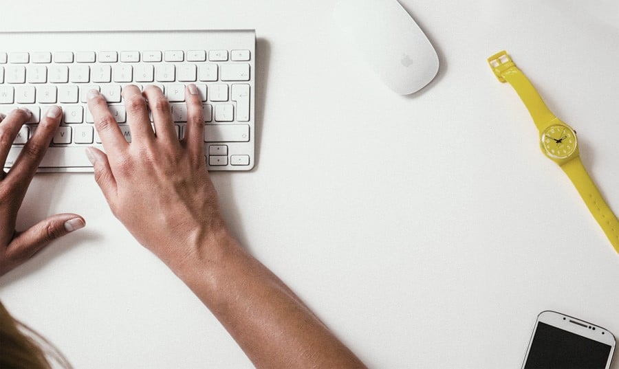 Foto de uma pessoa digitando em um teclado branco, em uma mesa branca, com objetos ao lado. , executiva, pensando...