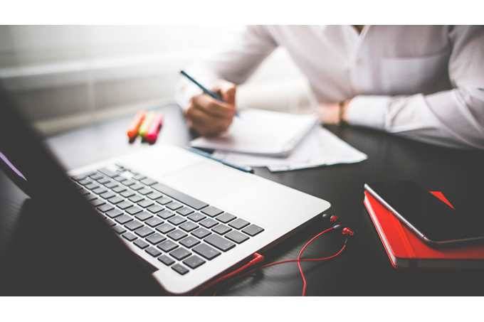 Foto de um homem apoiado em uma mesa com cadernr e notebook, escrevendo no caderno - pensando nos benefícios do empreendedorismo digital no Brasil